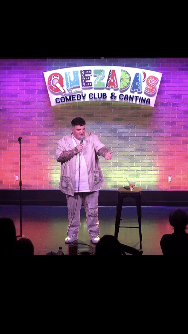AJ Deleon standing on stage doing standup comedy